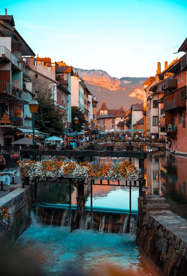 Flower-decorated canal bridge in Annecy with colorful buildings and mountain backdrop