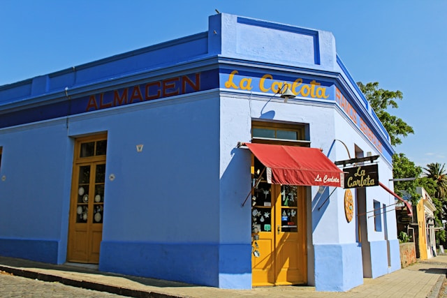 La Carlota almacén, a bright blue corner general store with yellow doors and red awning in Colonia del Sacramento