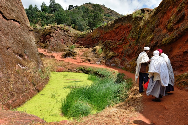 Ethiopian Orthodox priests in white robes walking through a narrow rock-cut passage in Lalibela