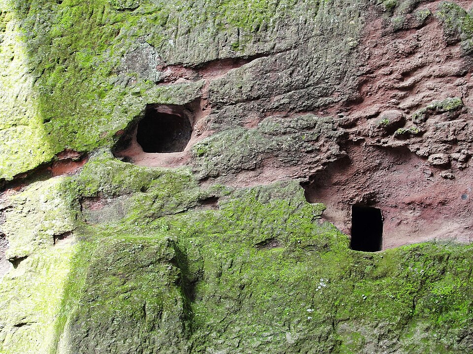 Moss-covered volcanic rock face with carved openings at the Lalibela church complex