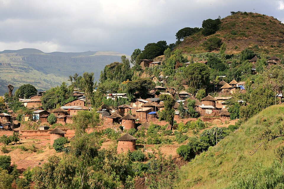 Hillside village near Lalibela with traditional round tukul homes and highland mountains in the background