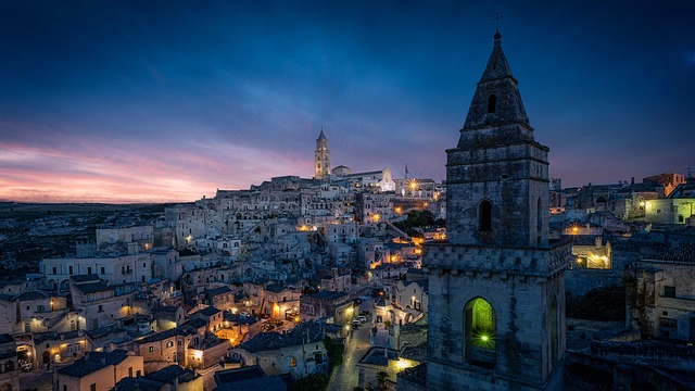 Evening view of Matera's illuminated stone buildings and church towers under a colorful twilight sky