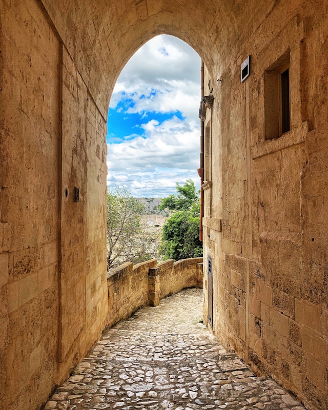 Narrow cobblestone passage beneath a stone archway in Matera with views of trees and the surrounding landscape beyond
