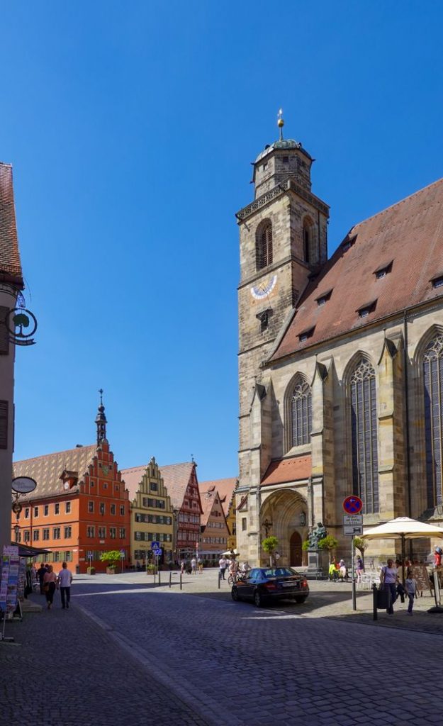 Gothic church with a tall tower beside a sunny town square in Germany