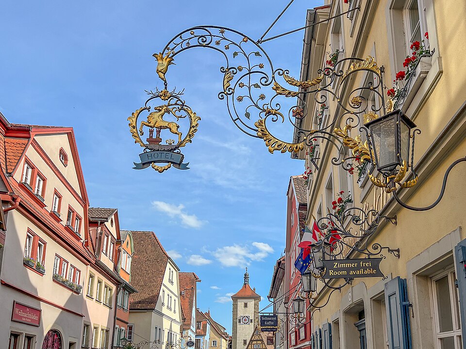 Ornate golden stag hotel sign over a Rothenburg street with a tower in the distance
