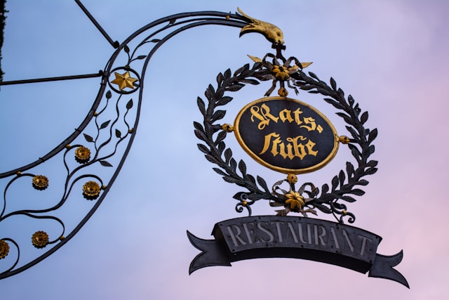 Ornate wrought-iron Rats-Stube restaurant sign against a dusk sky in Rothenburg ob der Tauber