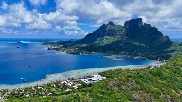 An elevated view over a bright turquoise lagoon bordered by a motu and coastal road in Bora Bora French Polynesia