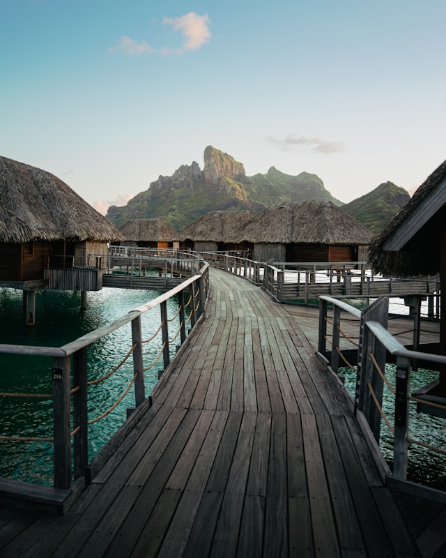 Weathered wooden boardwalk leading toward a row of thatched-roof huts over turquoise water in Bora Bora French Polynesia