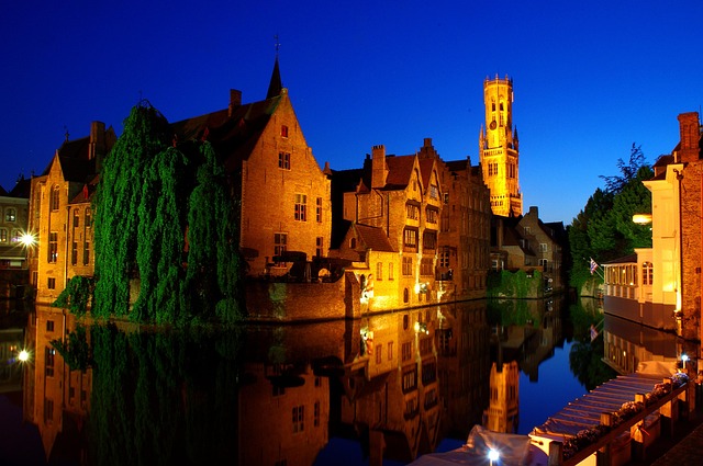 Bruges canal illuminated at night with the Belfry tower reflected in the water