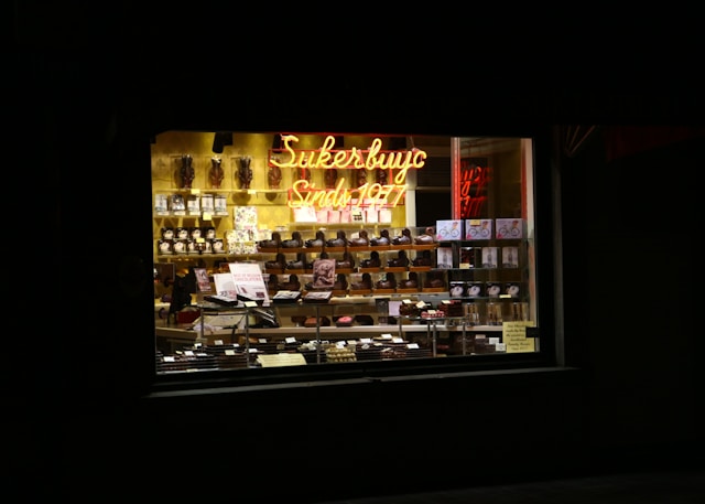 Illuminated candle display in a chocolate shop window at night