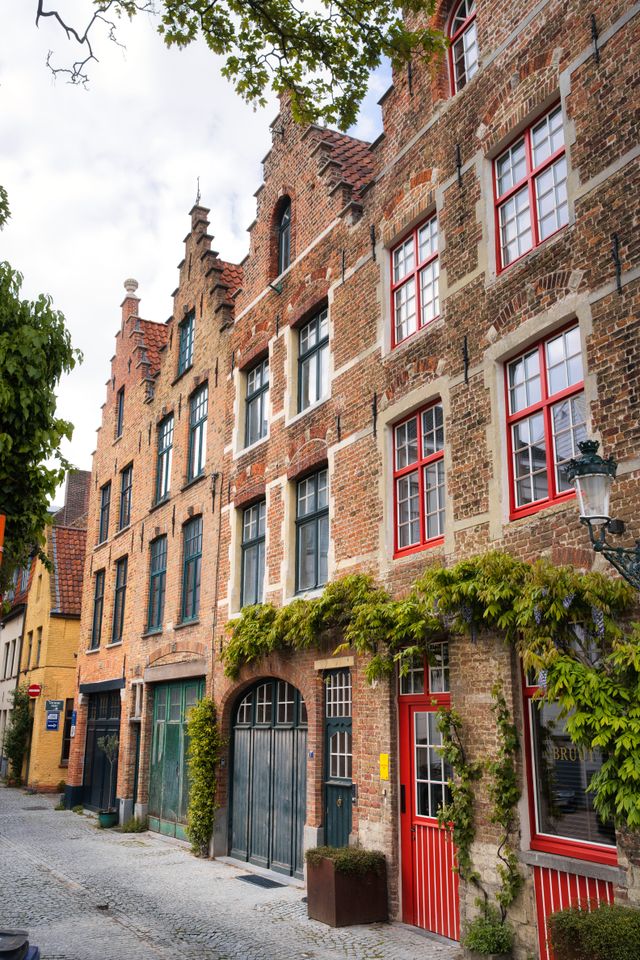 Row of medieval brick buildings draped in greenery on a Bruges street
