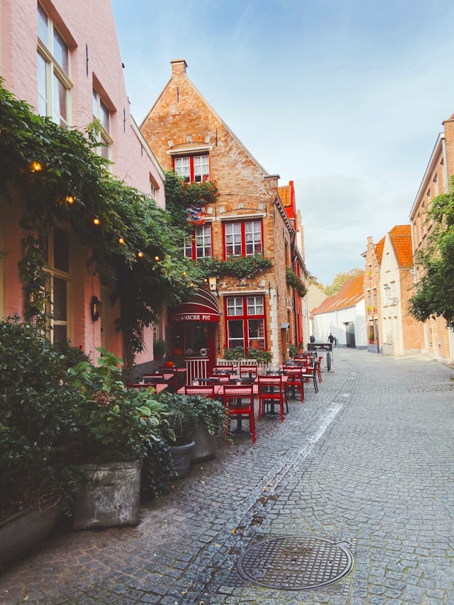 Cobblestone street lined with red cafe tables outside a restaurant in Bruges Belgium