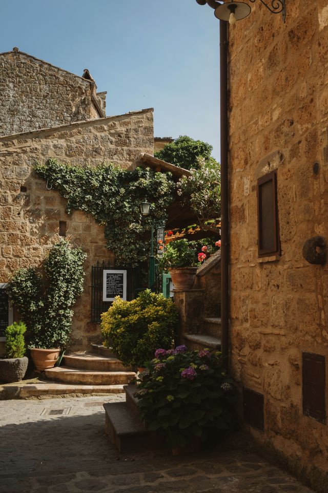 A shaded stone alley with greenery and a small chalkboard sign in Civita di Bagnoregio Italy