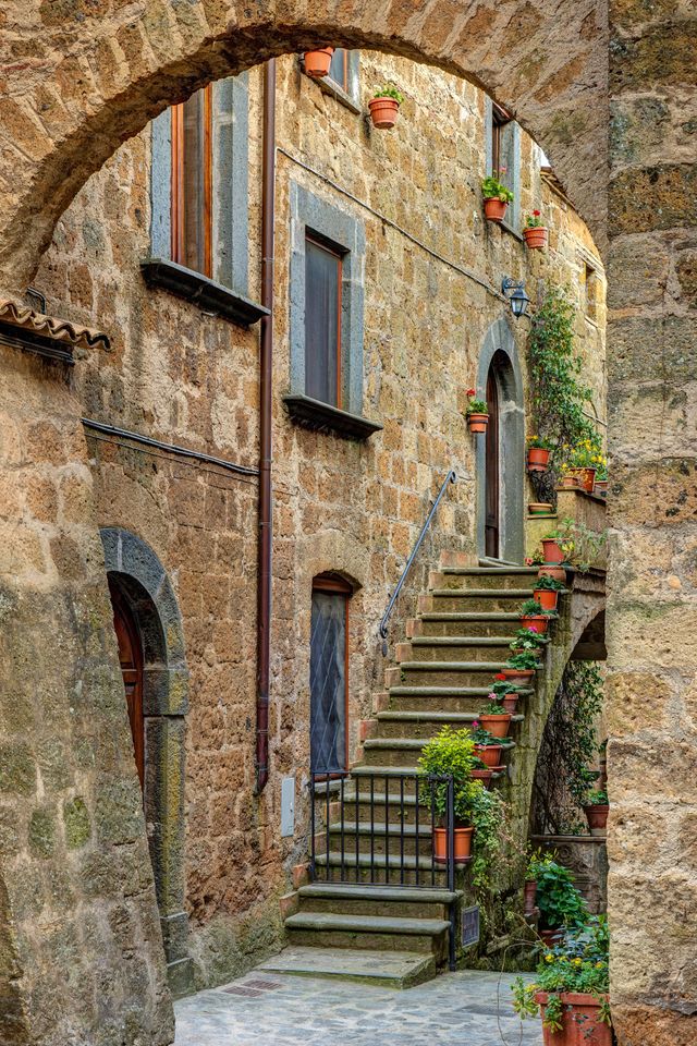 A stone archway leading to a staircase lined with potted plants in Civita di Bagnoregio Italy