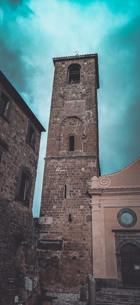 A tall stone bell tower with a clock rising above the village