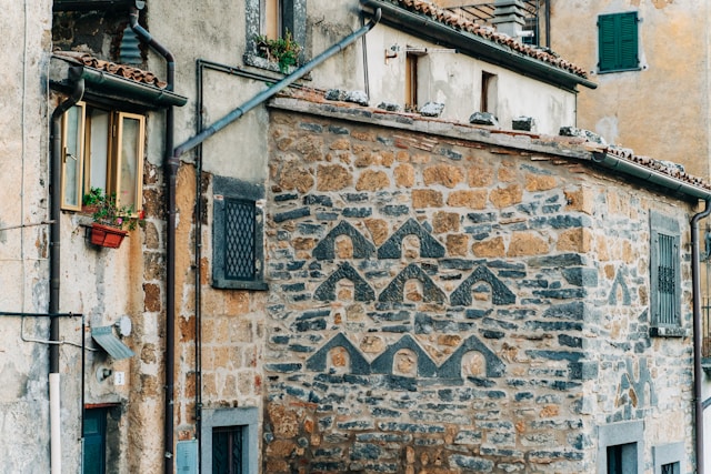 A weathered stone wall with a patterned brick design and a flower box window