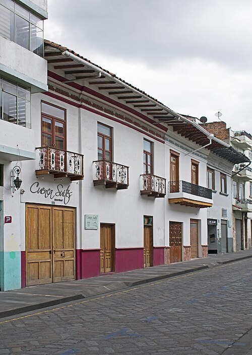 A row of white colonial buildings with wooden balconies along a quiet street