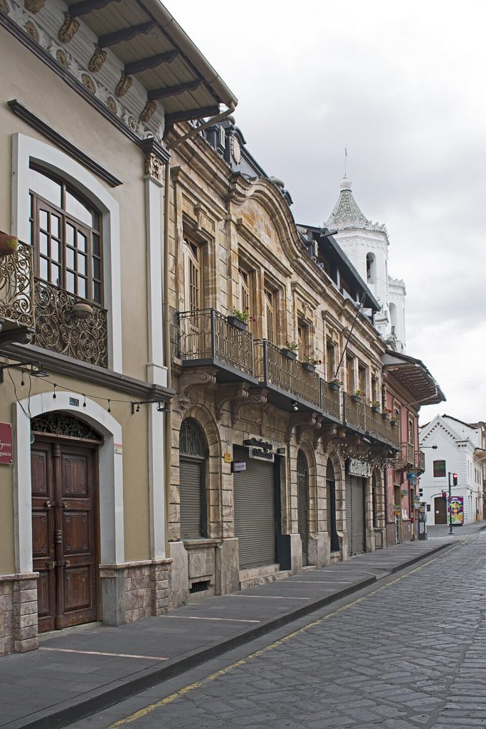 A colonial street corner with ornate ironwork balconies and a distant church tower