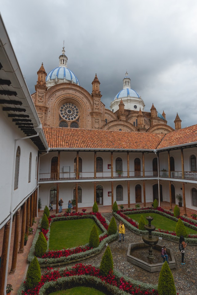 A manicured courtyard garden with a stone fountain framed by cathedral domes in Cuenca Ecuador