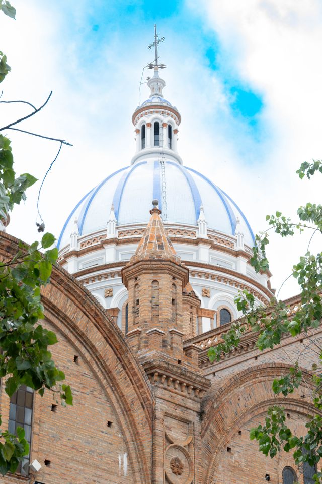 The cathedral's blue and white dome framed by tree branches in Cuenca Ecuador