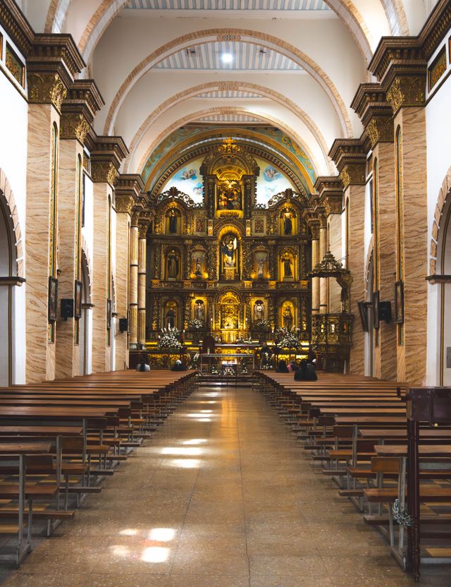 A gilded altar and rows of wooden pews inside the cathedral nave in Cuenca Ecuador