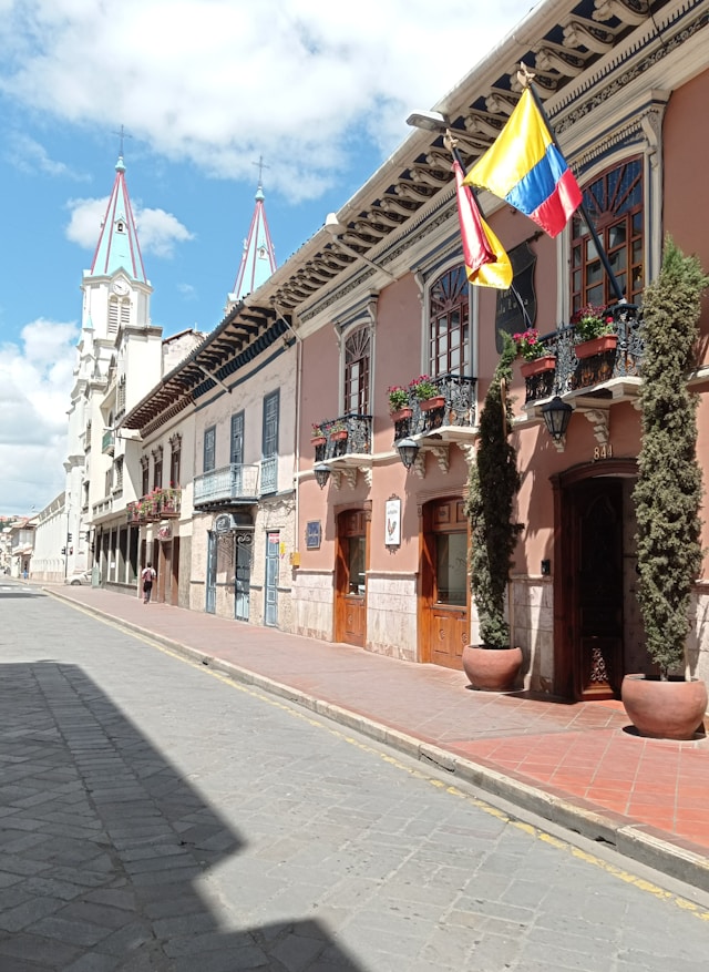A rose colored colonial facade with Spanish and Ecuadorian flags below twin blue spires