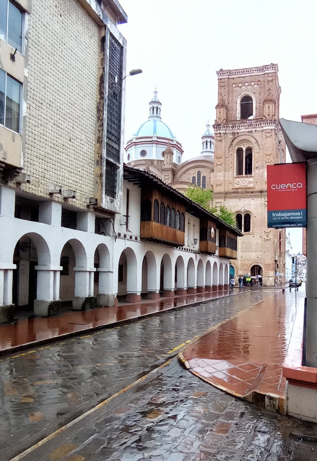 A rain slicked colonial arcade leading toward a brick cathedral tower in Cuenca Ecuador