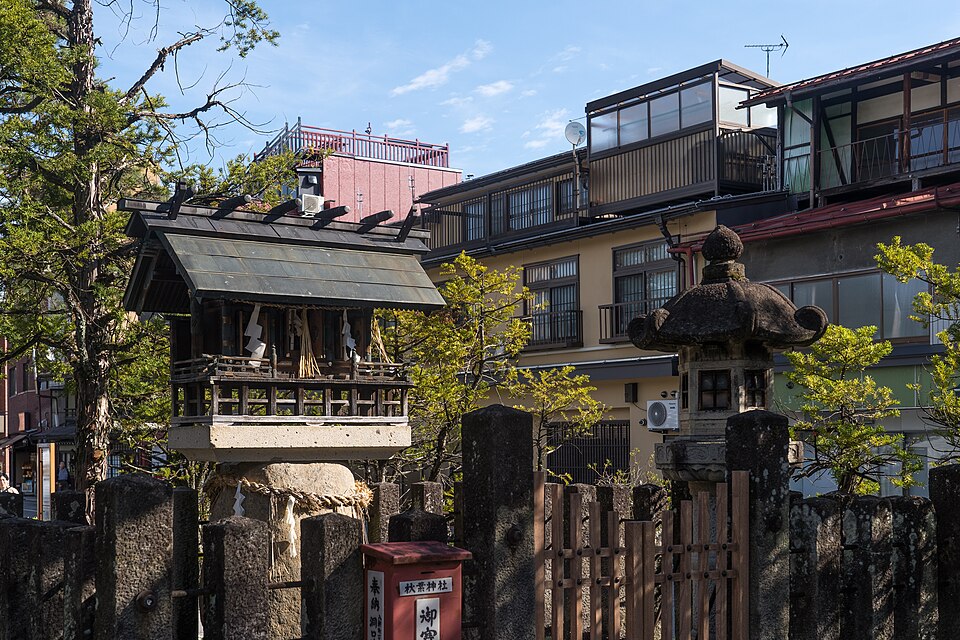 Small shrine building and stone lantern among Takayama's rooftops