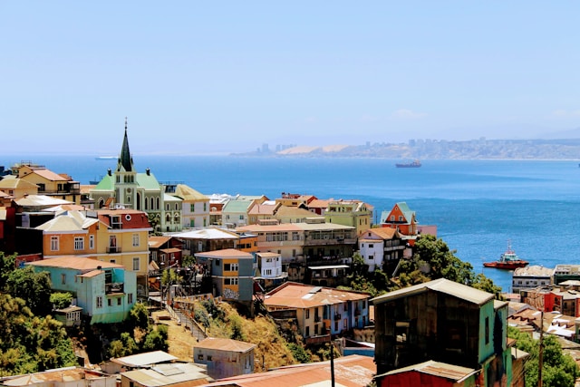 A hillside church spire in Valparaiso Chile overlooking a wide bay dotted with cargo ships