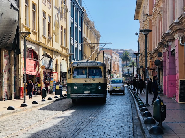 A vintage green and cream trolleybus rolling down a cobblestone city street