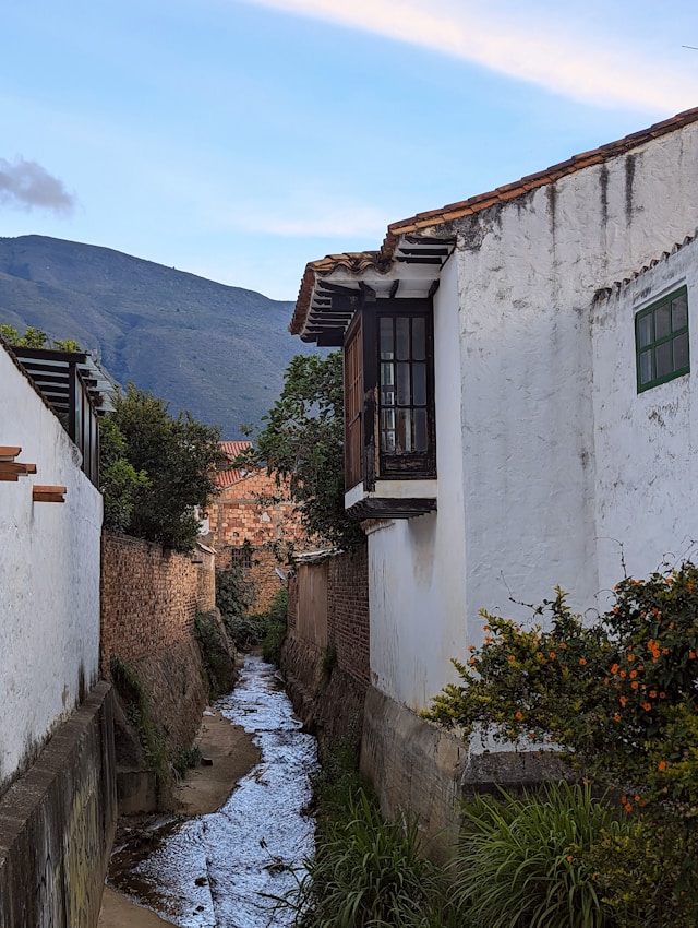 Narrow alley with a running stream between whitewashed buildings and mountains