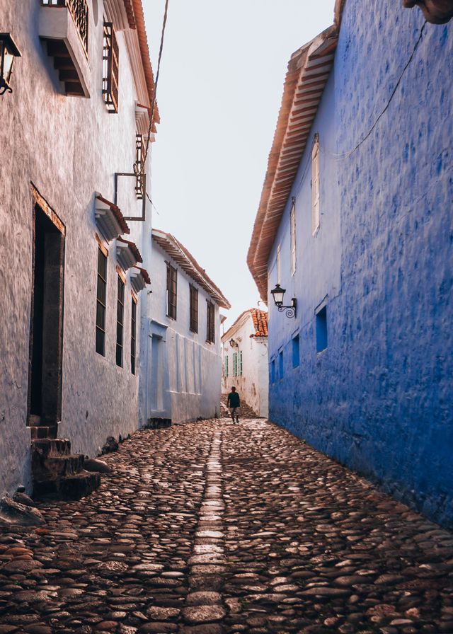 Narrow cobblestone alley between a blue and a white colonial building in Villa de Leyva Colombia
