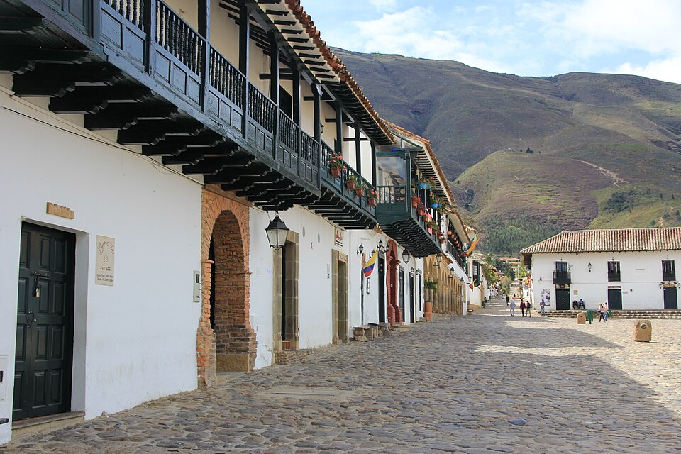 Long cobblestone street lined with colonial buildings beneath green mountains
