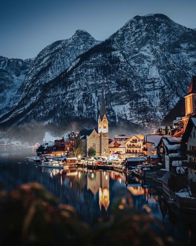 Hallstatt's illuminated church tower reflected in the lake at blue hour beneath snow covered peaks