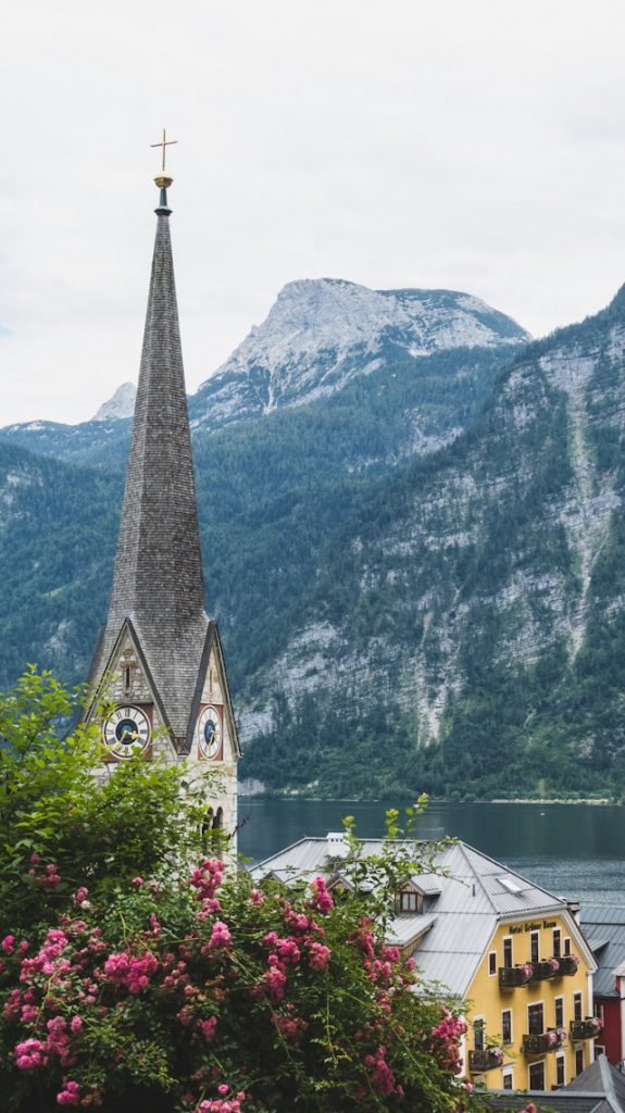 Hallstatt's church clock tower rising above pink roses with the lake and mountains beyond