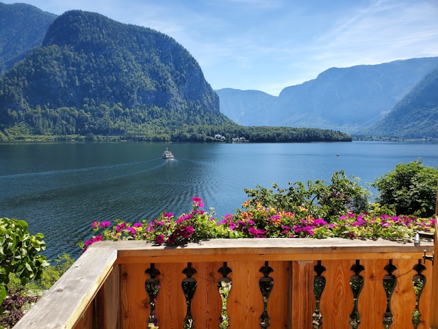 Pink petunias on a wooden balcony overlooking Lake Hallstatt with a passing boat