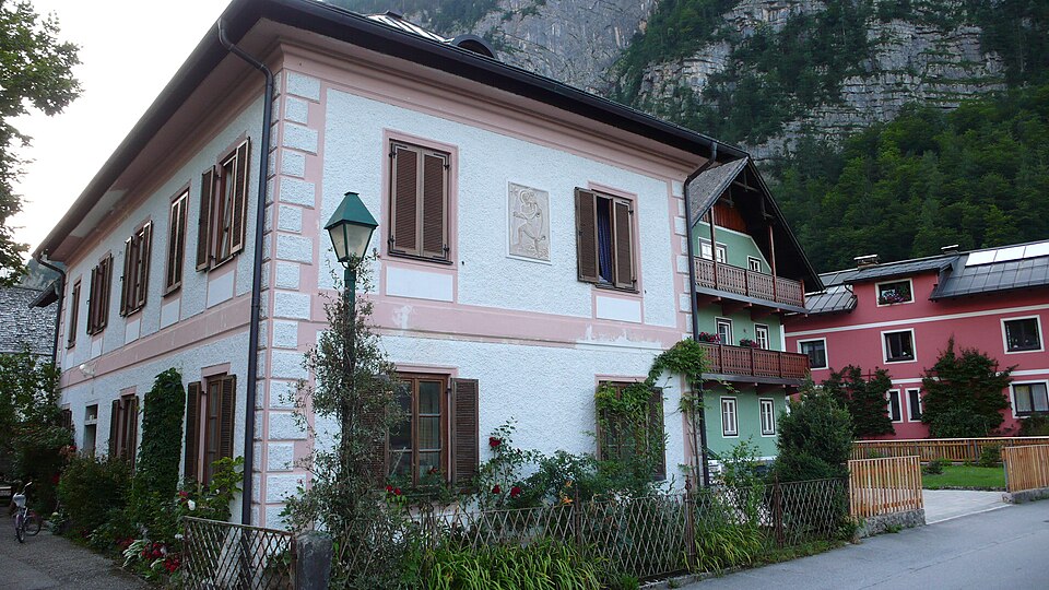 A pink corner house on Salzbergstraße in Hallstatt with mountains behind