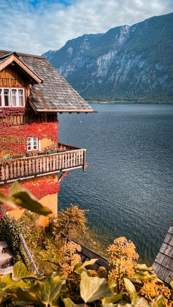 A yellow lakefront house covered in red autumn vines above Lake Hallstatt