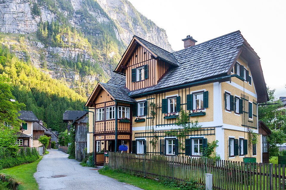 A yellow house with green shutters beneath a mountain in Hallstatt
