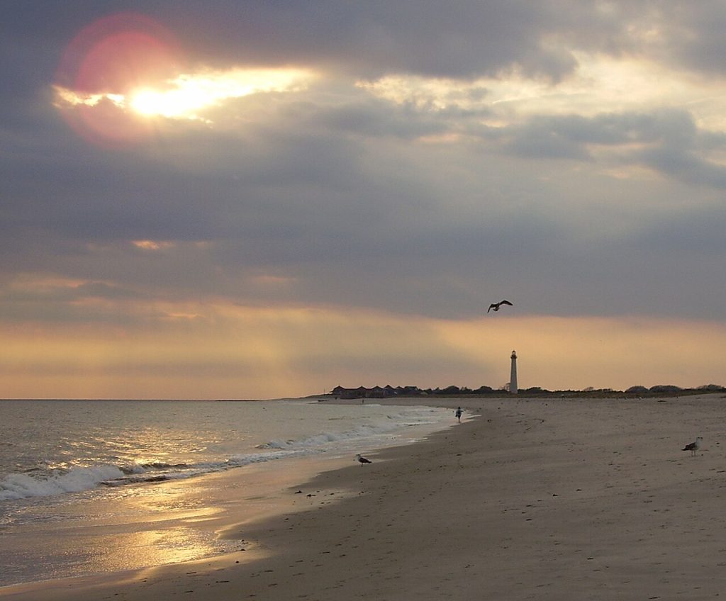 A calm beach at sunset with a lighthouse in the distance