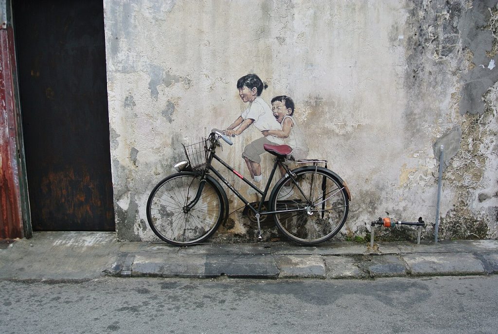 A street mural of two children riding a real bicycle