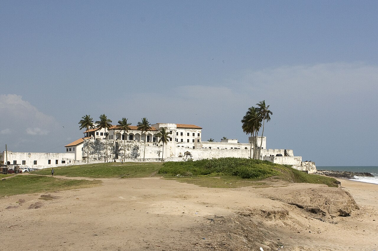 Whitewashed Elmina Castle beside a harbor full of boats