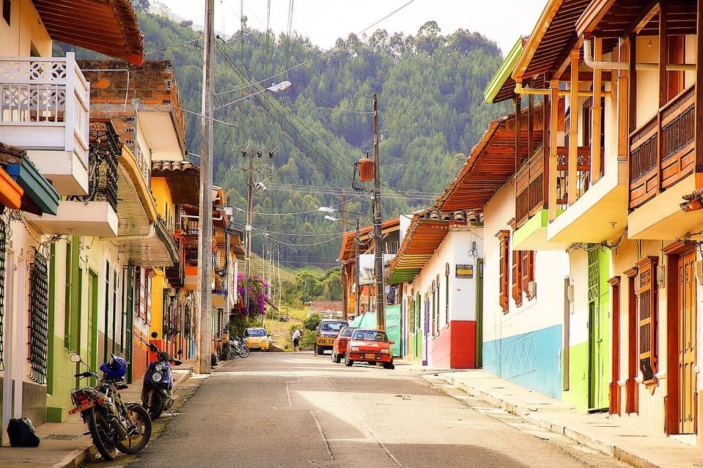 Colorful houses with wooden balconies lining a street in Jardín, Colombia, with green mountains behind