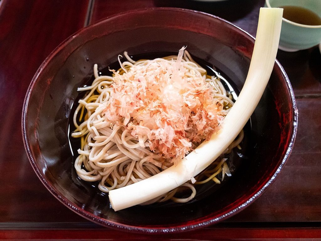 A bowl of soba noodles topped with grated radish and bonito flakes