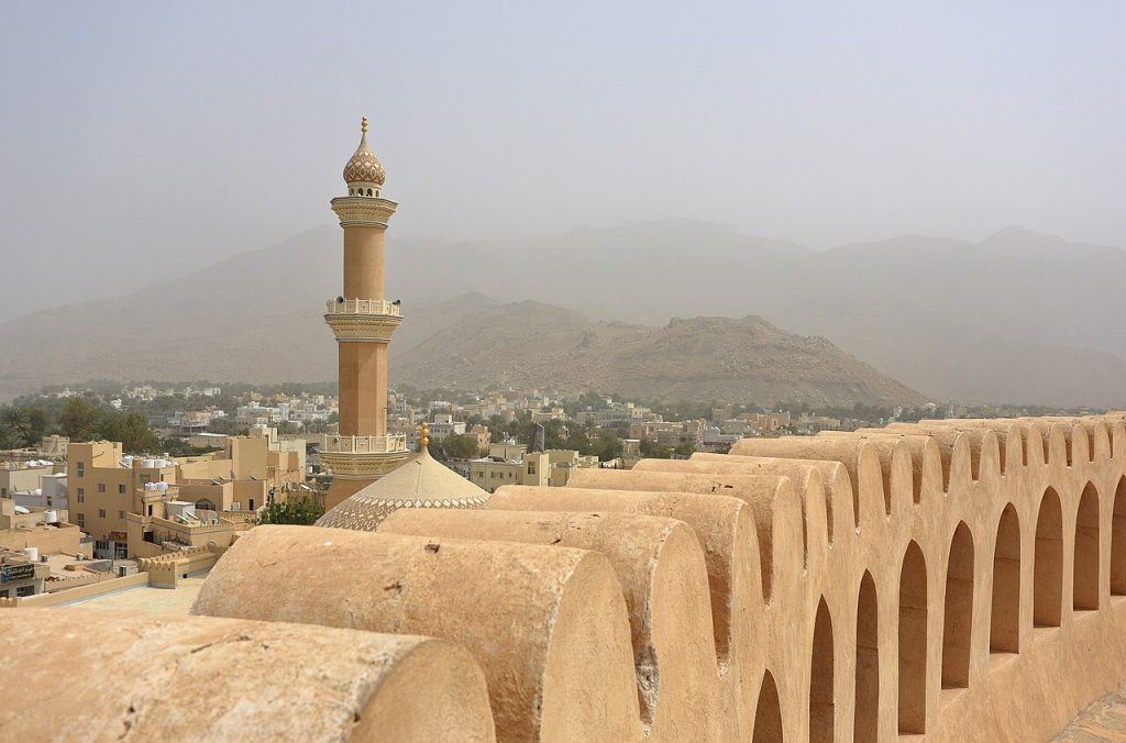 Nizwa Oman fort walls with a mosque minaret and mountains behind