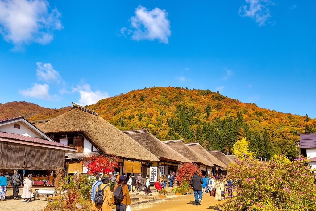 Thatched houses framed by red and orange autumn leaves