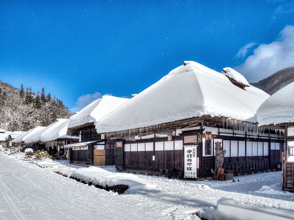 Snow-covered thatched houses in Ouchi-juku with mountains behind