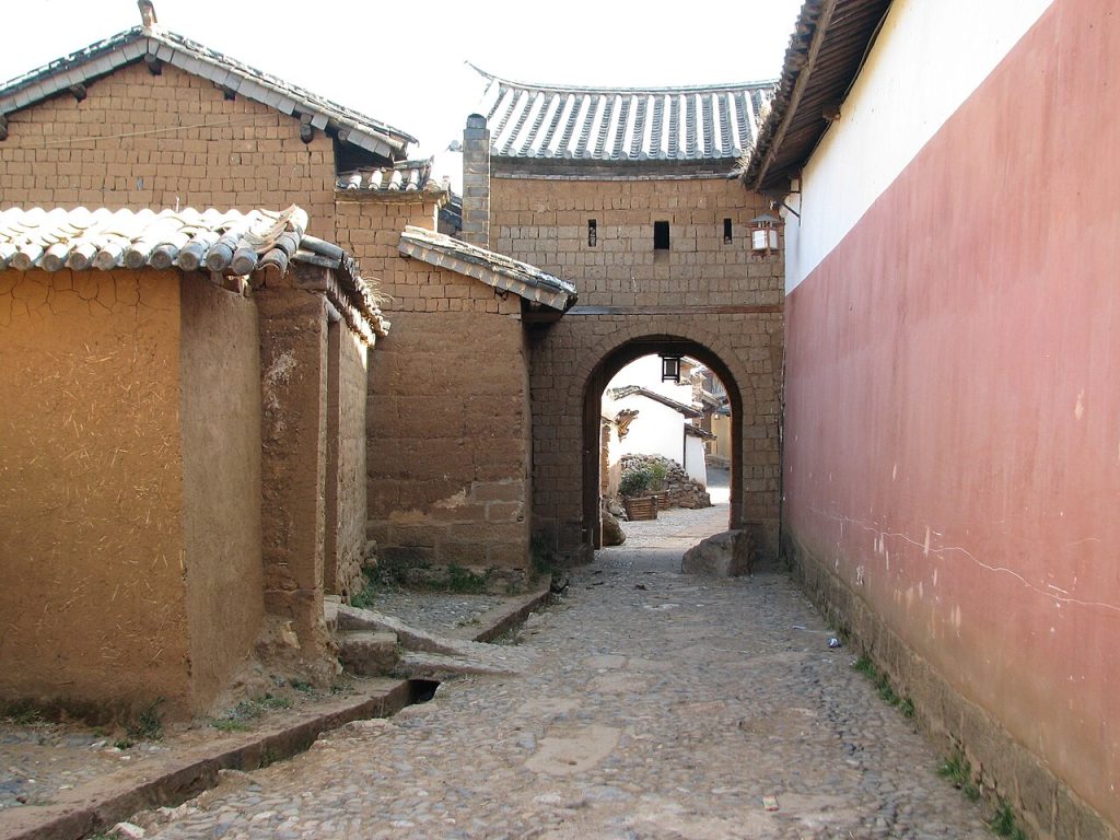 An arched gate in an earthen wall along a narrow village lane