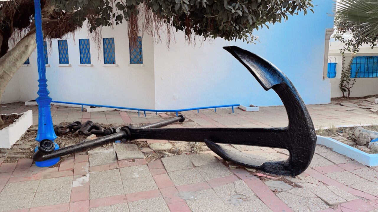 Old ship anchor beside white walls with blue windows